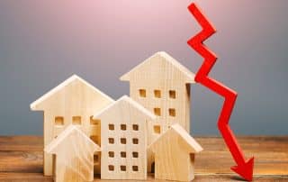 Holzhäuser mit fallendem roten Pfeil als Symbol für sinkende Immobilienpreise