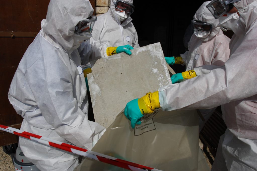 Arbeiter in Schutzanzügen entsorgen Asbestplatte mit Handschuhen und Atemschutz