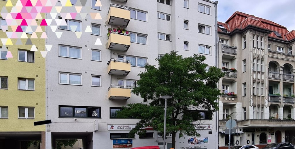 Fassade eines Mehrfamilienhauses in Berlin mit gelben Balkonen und Ladengeschäften im Erdgeschoss