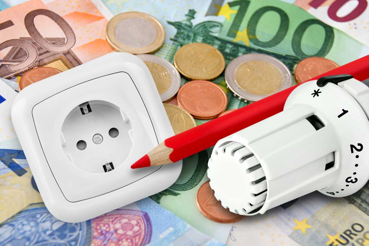 Thermostatventil, Steckdose und roter Stift liegen auf Euro-Banknoten und Münzen