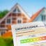 Energieausweis mit farbiger Effizienzskala vor einem Wohnhaus im Hintergrund